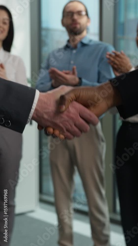 Two businesspeople shaking hands handshake agreement deal contract client director success diversity happy workers in background applaud congratulations celebrate office business company partnership