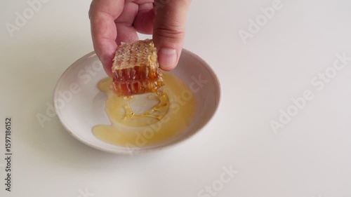 A man's hand takes a piece of honeycomb with honey from a saucer.