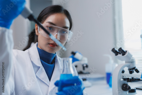 Scientist using pipette dropping liquid into beaker in laboratory