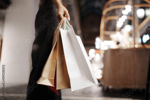 Stylish young woman walking outdoors at night, carrying shopping bags with joy, surrounded by city lights, fashion, and festive retail vibes.
