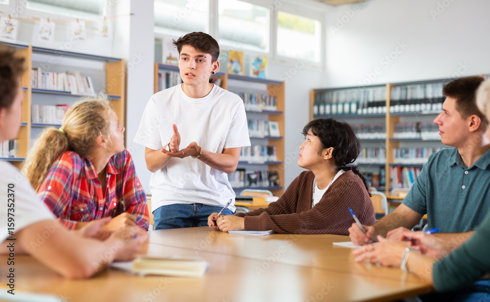Fototapeta premium Guy tells an interesting story to his friends in the school library