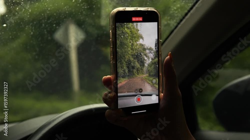 Young woman driving and filming scenic jungle road with smartphone holding in one hand, Northern Thailand.