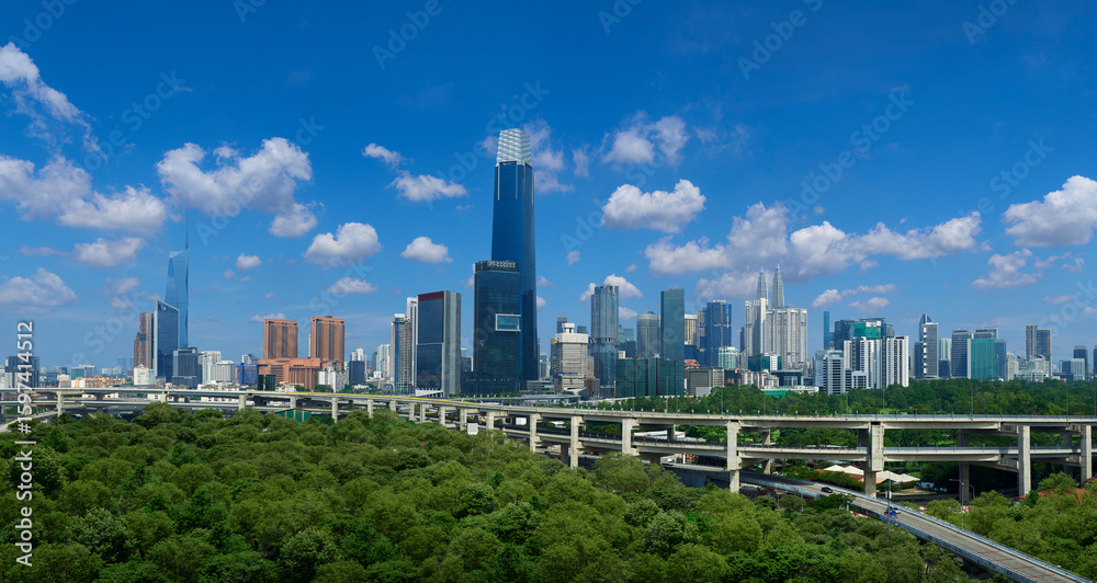 Obraz premium Kuala lumpur skyline rising above lush green forest and elevated highway on sunny day