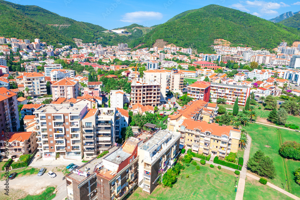 Obraz premium Aerial view of Budva, Montenegro, featuring a vibrant town with colorful buildings nestled between green hills and mountains. Landscape with modern and traditional architecture and lush greenery 