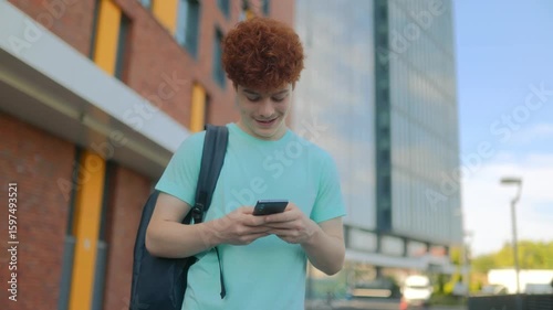 Happy redhead teen smiling while texting outdoors in casual outfit