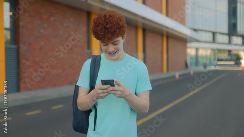 Happy teen schoolboy using smartphone with casual style in city