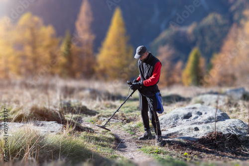 Man on a treasure hunt with a recreational metal detector in mountain pasture, at sunrise and with autumnal color. Electronic treasure finder. Blurred background and copy space