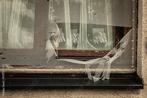 Broken window with torn curtain revealing a glimpse into a forgotten space filled with history and mystery