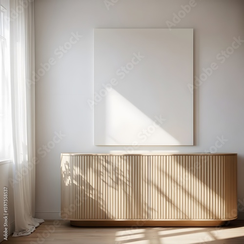 Sunlight streams through sheer curtains casting dramatic shadows across a modern slatted wooden cabinet with a large blank canvas artwork above it creating a serene and minimalist interior scene