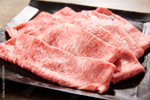 黒毛和牛の霜降りスライス肉を黒い角皿に美しく盛り付けたクローズアップ写真。艶やかな脂と繊細なサシ模様が際立つ高級食材のイメージカット。焼肉やすき焼きに最適。