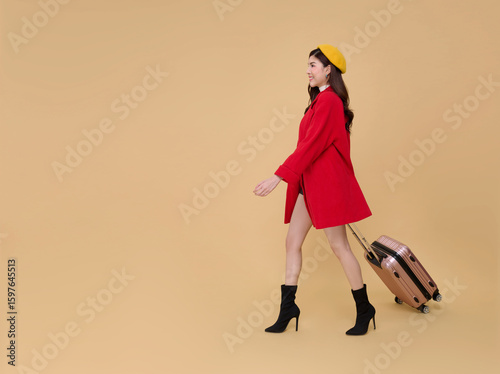 Happy young elegant Asian business woman travel holding luggage walking isolated on beige background. holiday business trip concept
