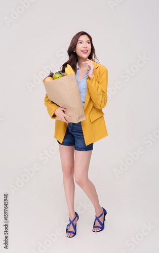 Happy Asian woman holding grocery shopping bag with food products looking up isolated on white background.