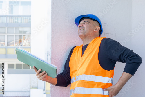 Injured construction worker or engineer suffering backpain. A warehouse worker in pain holding his back and making painful grimace