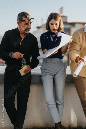A diverse group of business people reviewing project plans outdoors. The team is engaged and focused, illustrating collaboration and teamwork in a modern business environment.