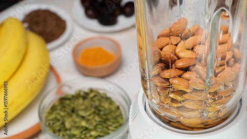 Slow motion pouring of clean water into blender with almonds. Flowing water over almonds inside glass blender. Vegetarian almond milk base for plant-based vegan and vegetarian smoothies and drinks.