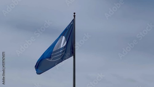 A Blue Flag, symbolizing high environmental and quality standards for beaches and marinas, proudly waves against a cloudy sky.