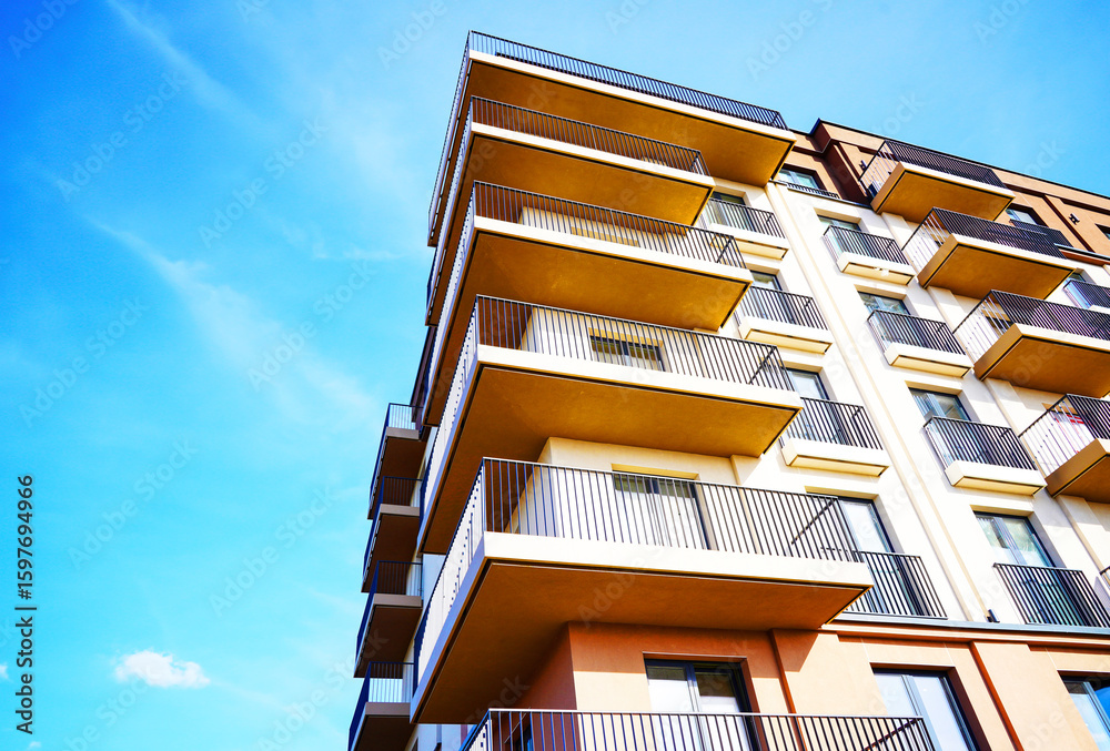 Fototapeta premium Balconies on blue sky, view up. New Apartment facade. Modern residential facade with balcony, windows. Architecture building exterior, house block. High Rise facade background. Modern housing estate.