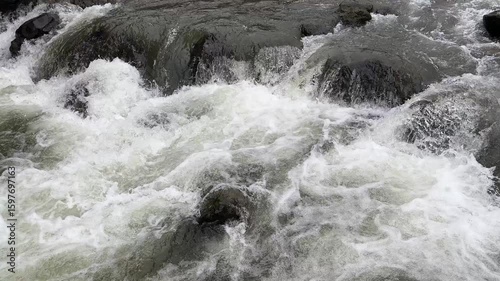 Fast flowing mountain river with clear water rushing over large rocks and boulders. Clear and natural river water in the countryside. Scenic natural landscape in the countryside.