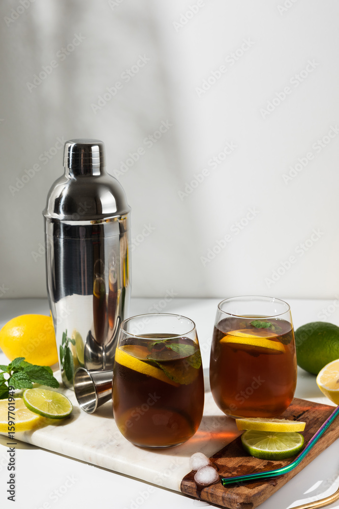 Glass cups and a jug of lemon and lime iced tea on a white table. Sunny day and sharp shadows from glass of lemonade Glass cups and a jug of lemon and lime iced tea on a white table. Sunny day and sharp shadows from glass of lemonade