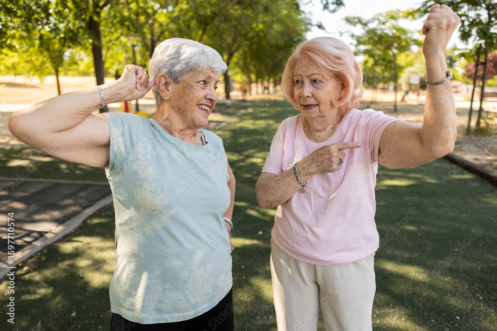 Fototapeta premium Two senior women showing their biceps in a park