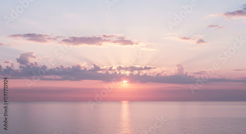 A peaceful view of the sunset over the ocean with soft pink and purple clouds above water
