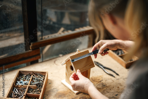 Fotografía Female artisan measuring wood to make homemade birdhouse, surrounded by vintage