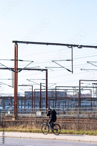 Commuter on bicycle passing train tracks in Copenhagen, Denmark, showing intermodal transport integration, everyday mobility and clean energy transit solutions in urban Europe