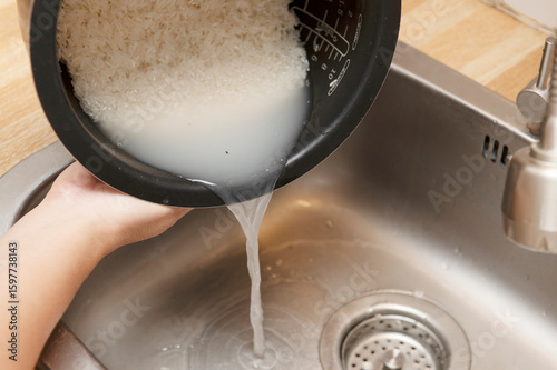 Slika na platnu Person rinsing raw white rice in a pot and pouring out cloudy water into a stain