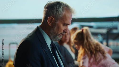 A pensive, middle-aged businessman with a gray beard looks down, possibly at a document or device, in a soft-lit office environment.