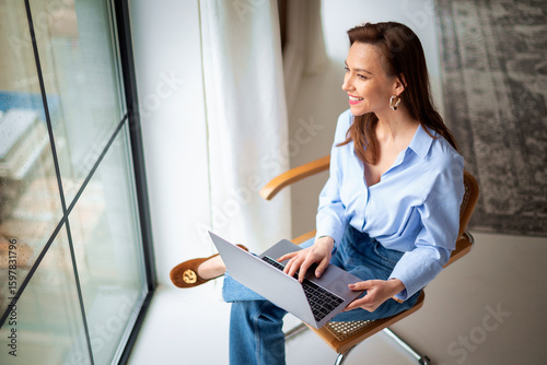 Attractive brunette haired woman sitting in a chair by the window in her apartment
