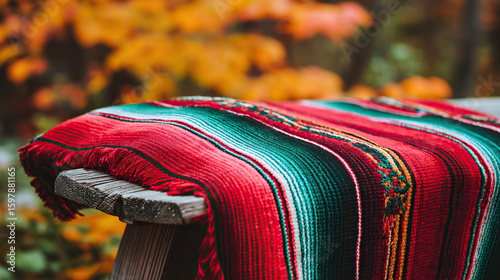 A traditional embroidered serape poncho in bold stripes of red, green, and white, draped over a rustic wooden chair with soft sunlight.