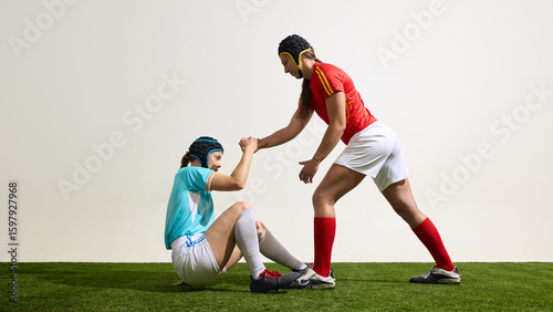 Photos Female rugby athlete helping another to get up on grassy field in match