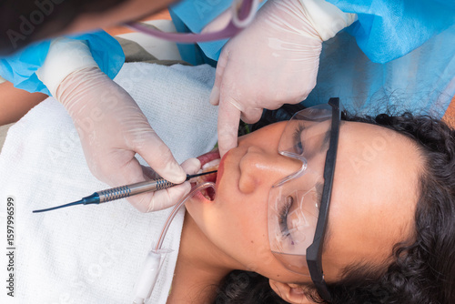Canvastavla Wide view of dentist applying composite filling to a lower premolar of a female patient wearing protective glasses during treatment