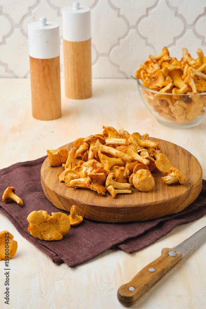 Fototapeta premium Fresh chanterelles on a round wooden board on a light concrete background. Wild mushrooms, gifts of the forest.