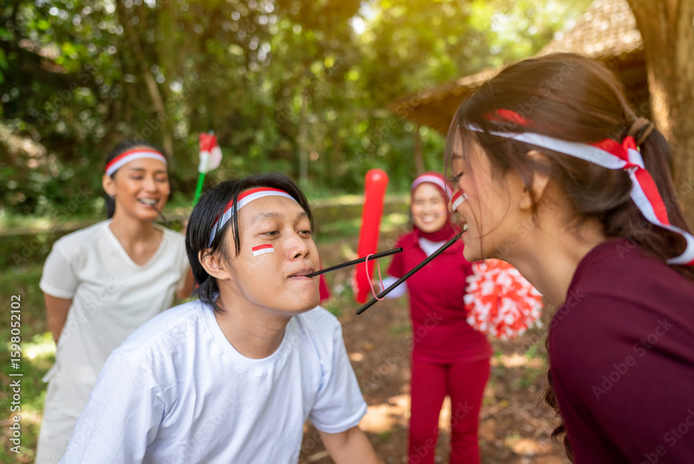 Fototapeta premium Portrait of Indonesian southeast asian people celebrate Indonesia Independence Day on the 17th of August with a game of moving the rubber band with a straw outdoors. Concept of Kemerdekaan Indonesia