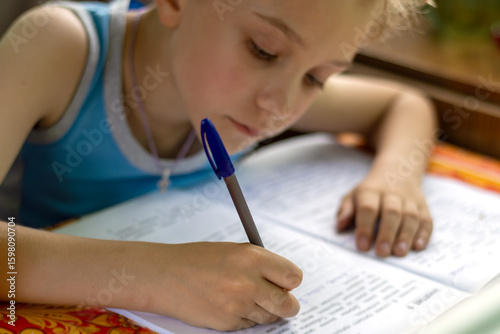 Photos Schoolboy concentrates on doing his homework during vacation on summer cottage terrace