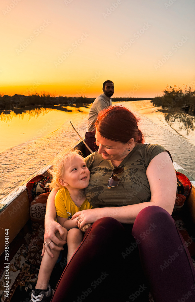 Fotobehang Chocoladebruin Tourist bonding with child on a boat in Iraqs picturesque sunset landscape #1598104144