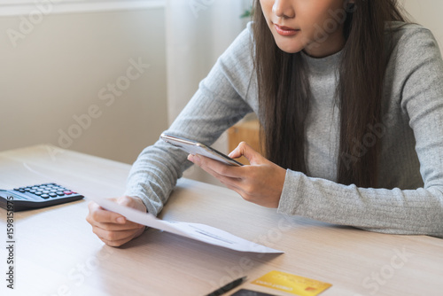 Bill pay concept. Online internet banking asian young woman hand holding invoice use mobile smart phone spend scan barcode to transfer to pay money of credit card without cash. Technology of financial