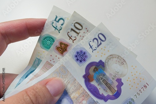 Fotografie Polymer banknotes of five, ten, and twenty sterling pounds are held by fingers a