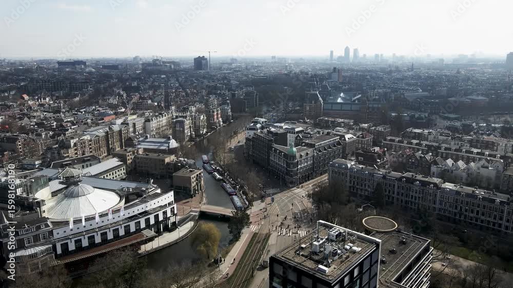Aerial view of the Rijksmuseum and canals, with buildings reflecting in the water under a hazy sky, Amsterdam, North Holland, Netherlands. Aerial view of the Rijksmuseum and canals, with buildings reflecting in the water under a hazy sky, Amsterdam, North Holland, Netherlands.