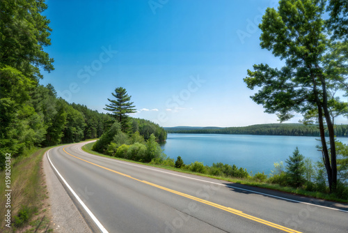 Serene summer road by peaceful lake with lush greenery and clear sky.