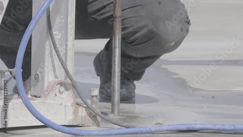 Slow-motion close-up of construction worker drilling hole into concrete rooftop using industrial equipment. Water and blue hoses visible. Ideal for industry, process, and infrastructure themes.