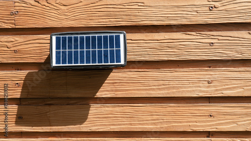 Small solar panel is mounted on wooden wall, casting shadow in sunlight. wood has textured, natural finish, adding rustic feel to scene