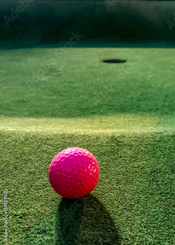 View from the turf of a pink golf ball and the hole on a miniature golf course