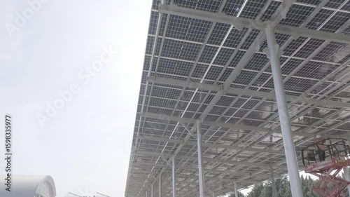Construction workers on aerial lift installing or maintaining large solar panel canopy structure. Renewable energy site. Filmed at solar energy project in Turkey.