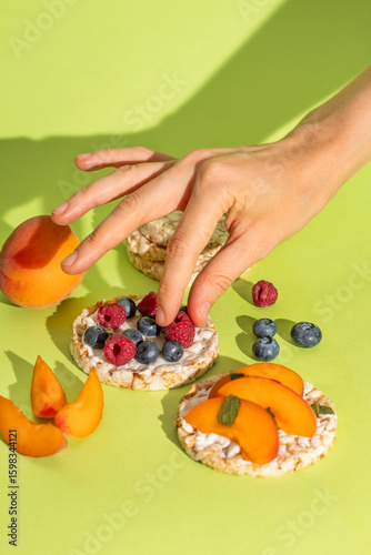 Rice cakes with different types garnish fruits, peaches, blueberries, apricots, raspberries with honey on green background. Healthy colorful food.