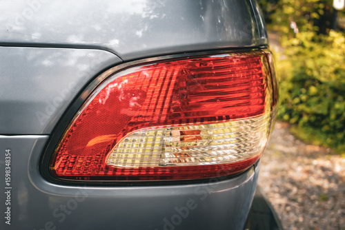 a brake light on a vehicle isolated against a driveway with green plants. red lens for the brake and running lights. transportation and safety background
