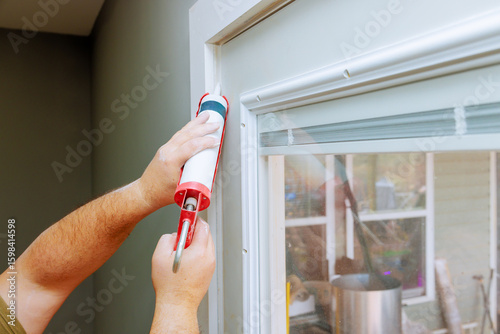 Contractor is using caulk gun to seal gaps around window frame during home improvement task.