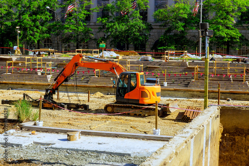 Construction activities are underway with an excavator operating on site surrounded by greenery building facades.