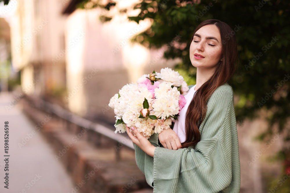 Fototapeta premium Charming woman with bouquet of beautiful peonies on city street. Space for text